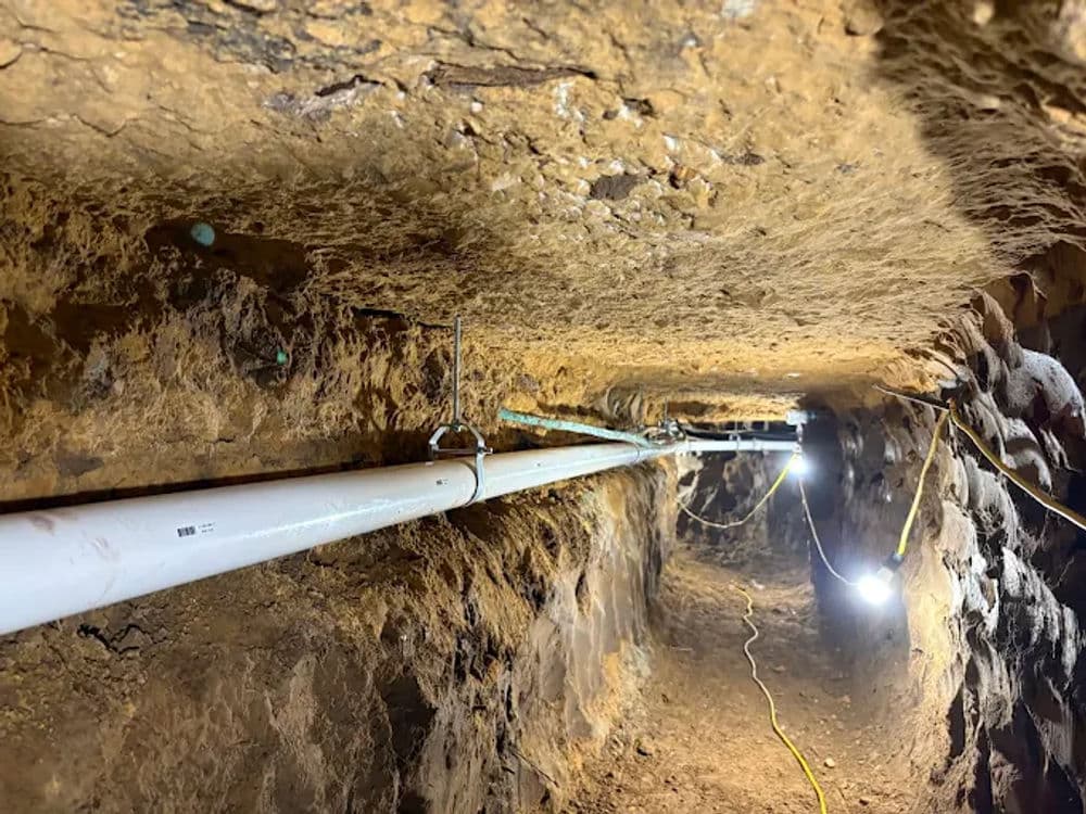 Underground tunnel with utility pipes and lighting, showcasing excavation details.