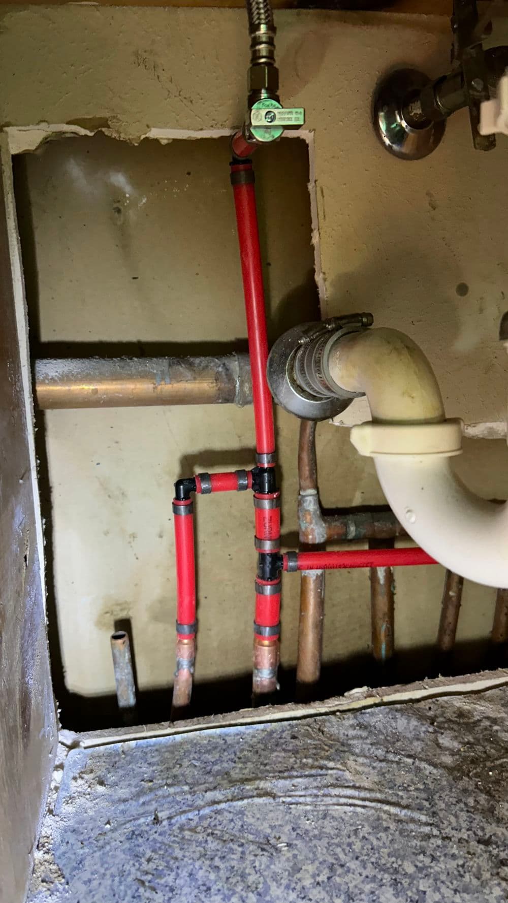Red and copper plumbing pipes under a sink, showcasing plumbing installation and repair details.