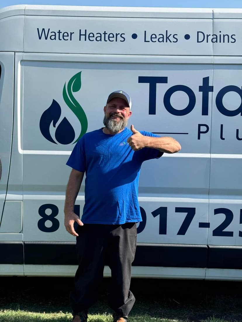 Man waving in a blue shirt in front of a service van with "Total Plumbing" branding.